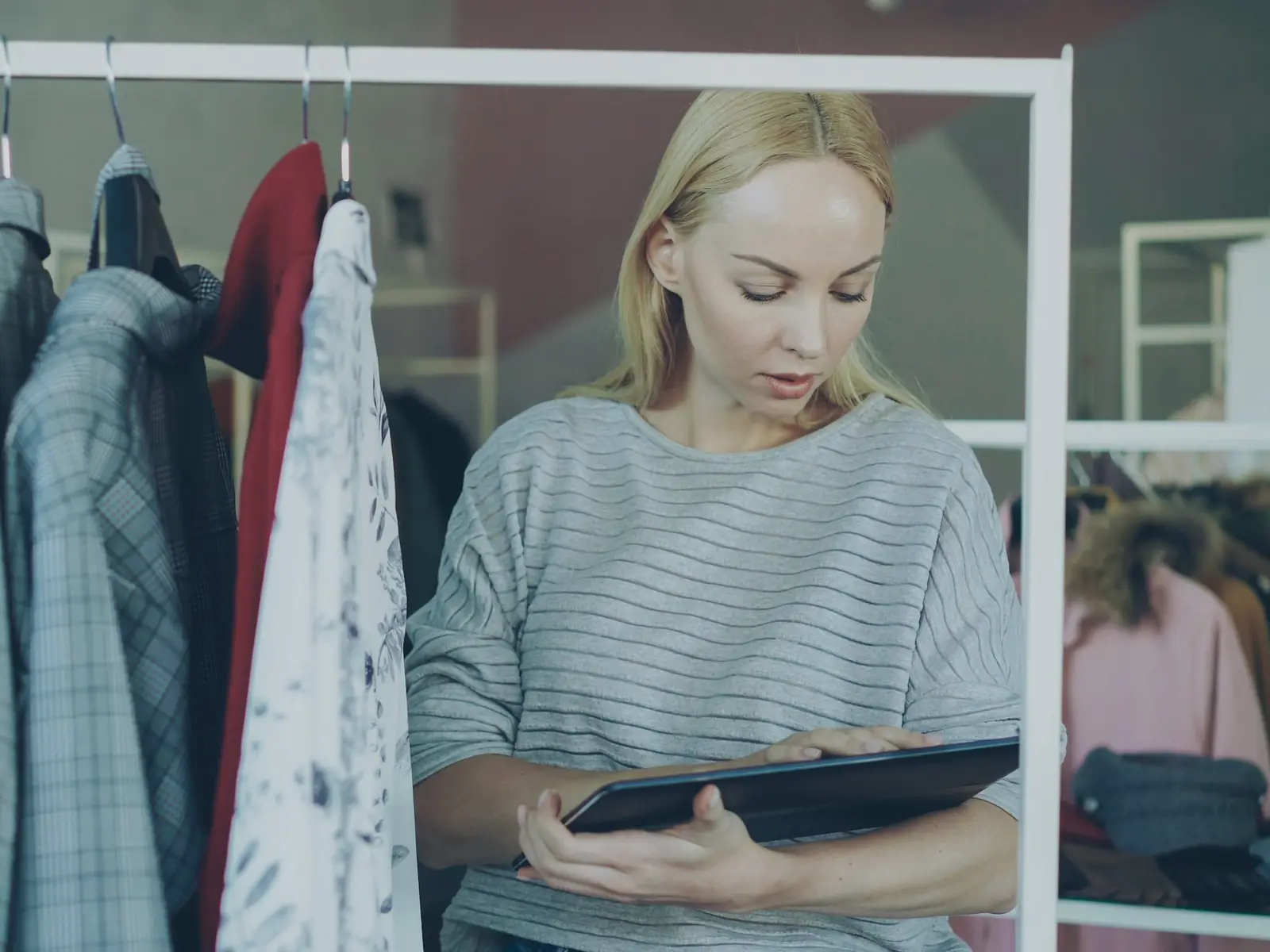 A woman checking a tablet beside a rack of clothing in a small shop